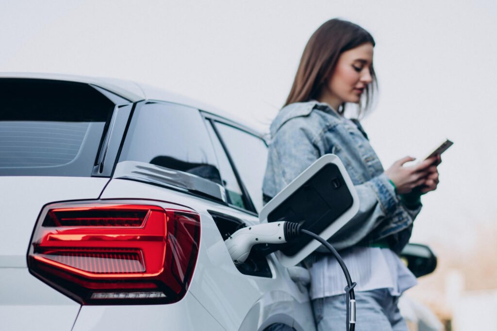 mujere cargando su auto híbrido mientras espera con celular